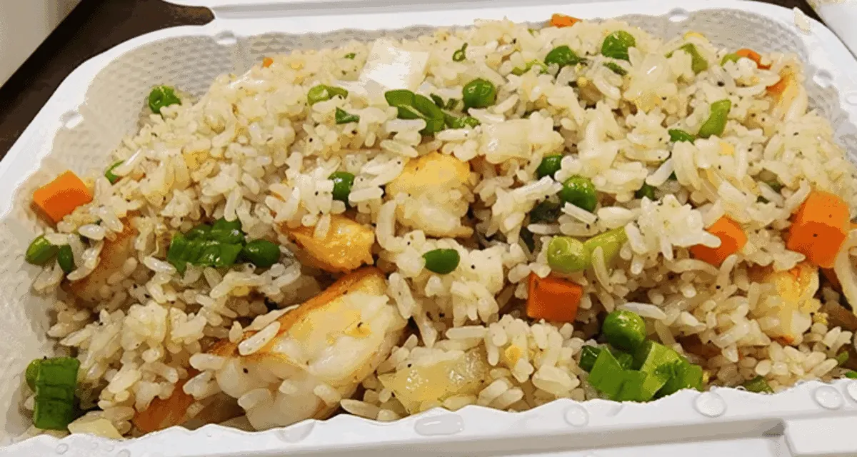A full takeout tray of fried rice with shrimp, peas and carrots.