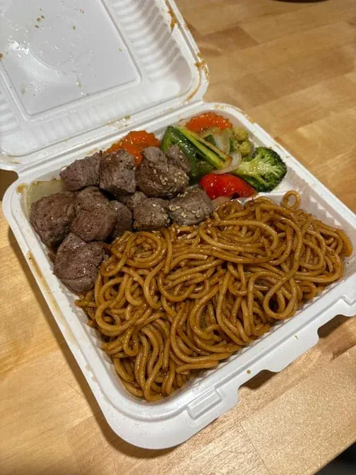 Hibachi steak with lo mein noodles and vegetables in a takeout box.
